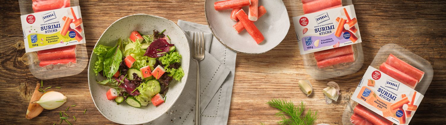 Drei Sorten Lysell Surimi auf einem skandinavischen Holztisch arrangiert. Als Sserviervorschlag ist eine Salat-Bowl zu sehen.