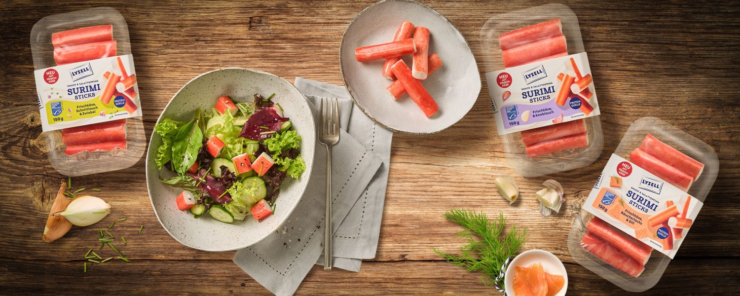 Drei Sorten Lysell Surimi auf einem skandinavischen Holztisch arrangiert. Als Sserviervorschlag ist eine Salat-Bowl zu sehen.